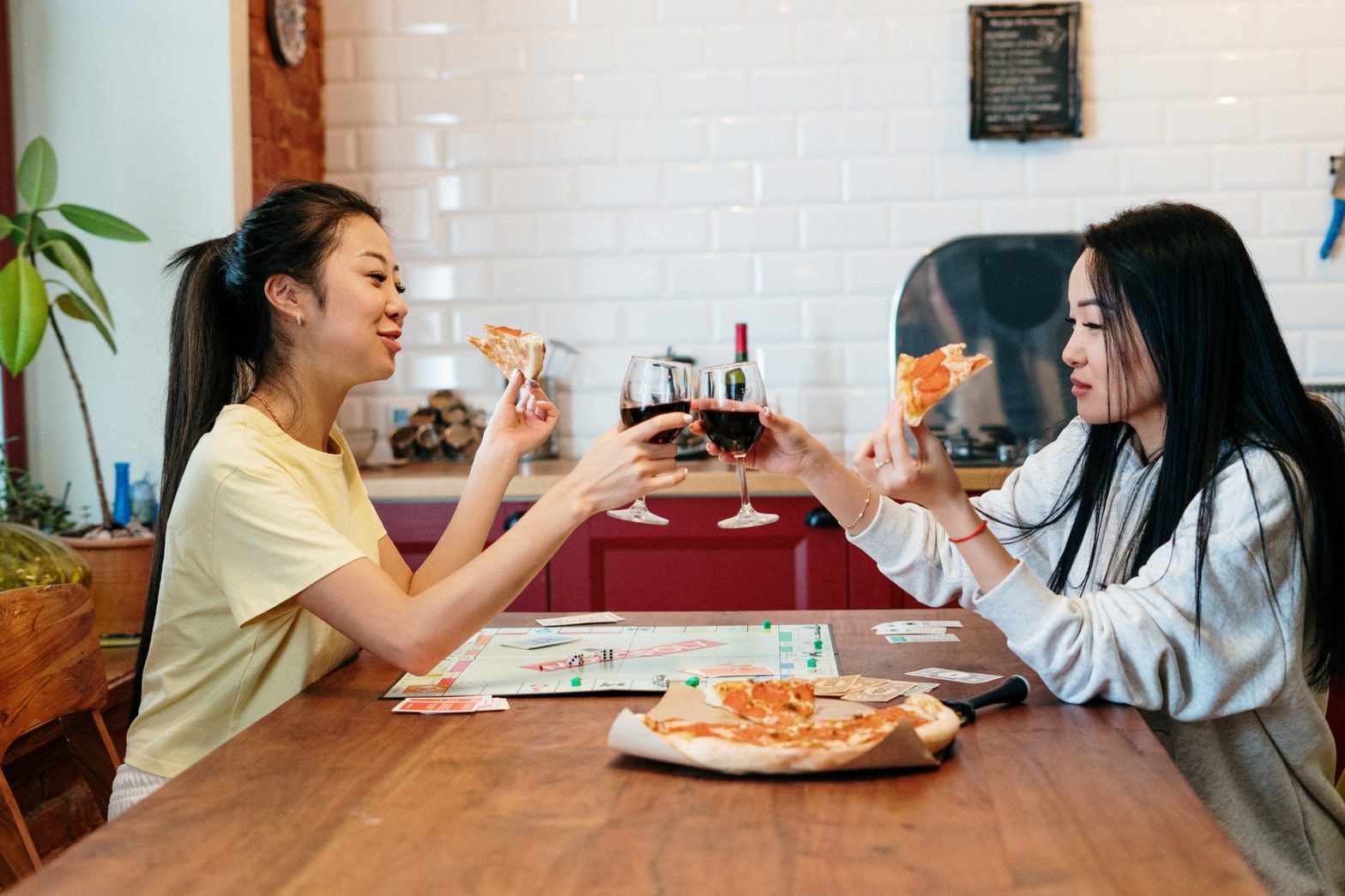 Two roommates sharing a glass of red wine and pizza